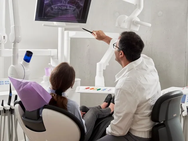 A dentist showing a patient a panoramic X-ray on a screen in a treatment room.